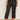 Someone wearing the Marine Jeans After Hours (extended sizing) by Sanctuary Clothing, featuring black cropped wide-leg style with front patch pockets, and black pointed-toe flats, stands against a light wall and concrete floor.