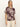 A woman with long blonde hair wears the Sanctuary Clothing sanc souvenir shirt mesa palm—a short-sleeved, button-up shirt with a bold beige palm leaf pattern on dark brown—paired with light pants against a plain backdrop.
