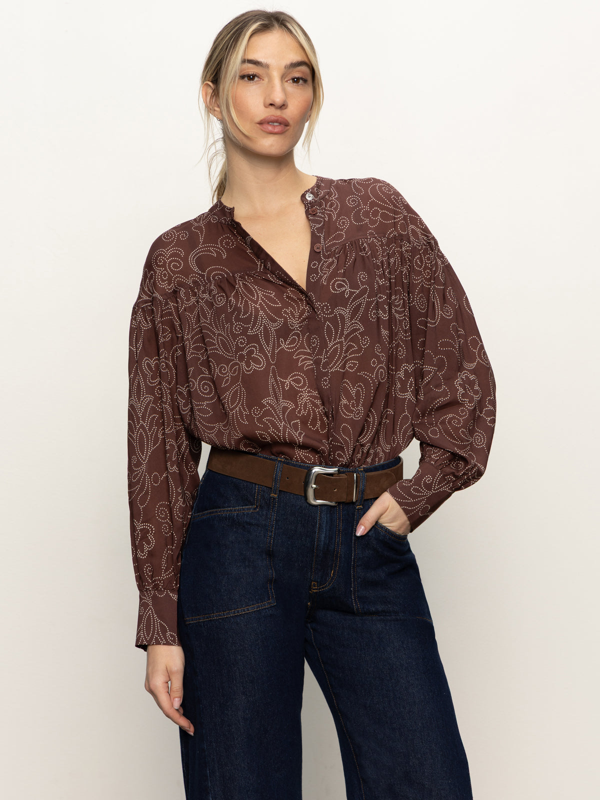 A woman models the Sanctuary Clothing personal best blouse boheme, paired with dark blue high-waisted jeans and a brown belt, against a plain light background.