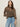 A woman with long brown hair models Sanctuary Clothing’s the adore blouse french kitty—a leopard print top with ruffled sleeves—paired with blue jeans, standing confidently against a plain light background.