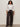 A woman with long curly hair wears the Sanctuary Clothing new era tuxedo shirt in white extended sizing, paired with loose dark brown satin pants. She stands facing forward against a plain light background, hands relaxed by her sides.