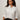 A woman with curly hair, wearing gold-rimmed glasses and black pants, models the Sanctuary Clothing new era tuxedo shirt white extended sizing against a plain light background with a neutral expression.