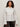 A woman with curly hair wears the Sanctuary Clothing new era tuxedo shirt white extended sizing with dark pants, standing against a plain light background.