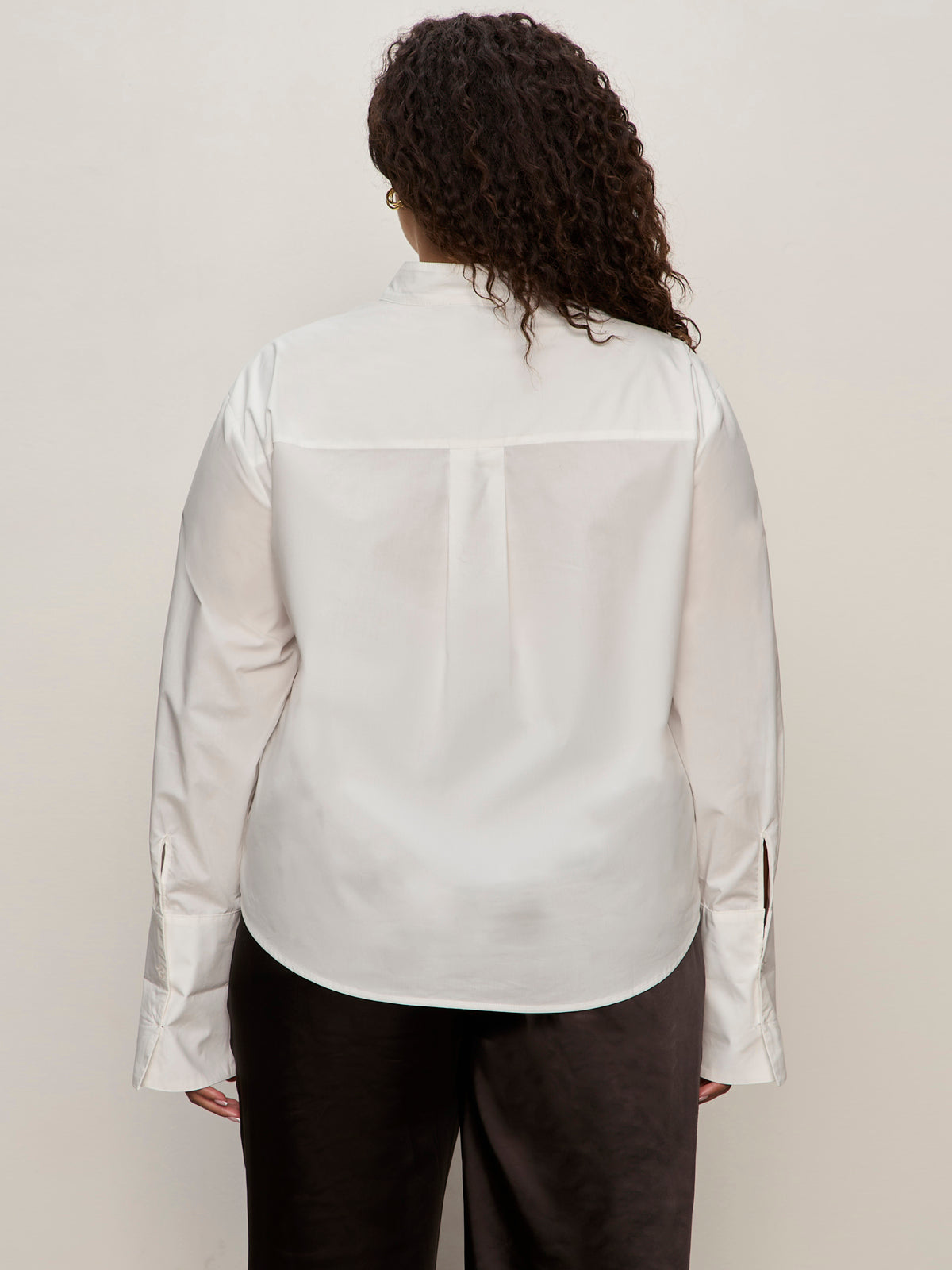 Seen from behind, a person with curly hair wears the Sanctuary Clothing new era tuxedo shirt white extended sizing and dark pants, standing against a plain light-colored background.