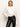 A woman with straight blonde hair models the Sanctuary Clothing new era tuxedo shirt in white, featuring wide cuffs, paired with black leather pants and one hand in her pocket against a plain white background.