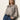 A woman with long, straight blonde hair wears Sanctuary Clothing's "wild dreamer blouse mother leo," a loose animal print top, tucked into high-waisted blue jeans with a black belt, standing against a plain light background and looking at the camera.
