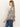 A person with long straight hair, wearing Sanctuary Clothing's wild dreamer blouse mother leo—featuring a black and brown animal print—and blue jeans, stands in profile against a plain white background.