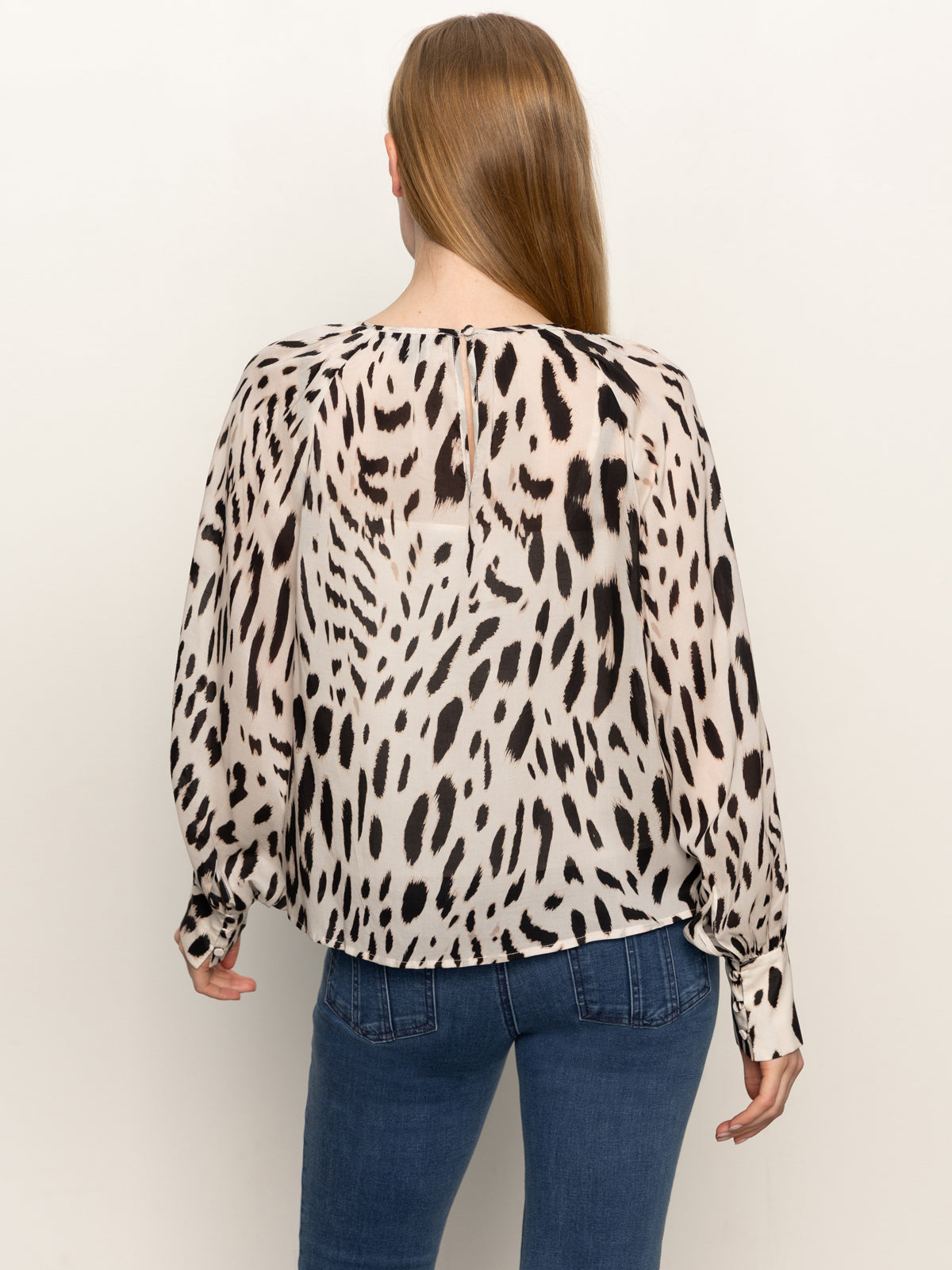 A person with long, straight brown hair is shown from the back, wearing Sanctuary Clothing’s wild dreamer blouse mother leo in a black and beige animal print and blue jeans.