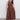 A woman with long dark hair wears Sanctuary Clothing's "take me away midi dress mesa" in extended sizing, featuring a sleeveless fitted top and gathered skirt, paired with black platform sandals. She stands on concrete before a plain light gray backdrop.