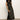 A woman with curly hair poses against a light wall, wearing the Sanctuary Clothing everyday satin dress in black olive and tan suede boots, with one hand on her hip.