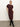 A woman poses against a plain light background, wearing the Sanctuary Clothing cinched waist t shirt dress in chicory, styled with black knee-high boots. She stands with one leg crossed and a hand on her hip.