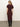 A woman with blonde hair in a low ponytail faces away, wearing the Sanctuary Clothing cinched waist t shirt dress in chicory with tall black boots against a plain light background.