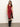 A woman in the Sanctuary Clothing revenge midi satin dress in crimson, featuring a sleeveless design and black lace-trimmed thigh-high slit, paired with knee-high black boots, stands against a plain light background.