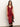 A woman wears the Sanctuary Clothing "revenge midi satin dress" in crimson, featuring a sleeveless V-neck, black lace-trimmed hem, and thigh-high slit, as she stands against a plain white wall.