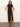 A woman stands against a plain light wall wearing Sanctuary Clothing's "Autumn's Best Sweater Dress" in cocoa plaid—a sleeveless, high-neck midi with a front slit—paired with knee-high tan suede boots.