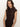 A woman with long brown hair wears the Sanctuary Clothing autumn's best sweater dress in cocoa plaid, featuring a sleeveless high-neck design. She stands against a plain light background, looking at the camera with a neutral expression.
