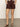 A person stands with hands in the pockets of Sanctuary Clothing's Renegade Short Mesa, styled with a patterned top and brown sandals against a plain light background.