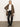 A woman stands against a white wall wearing the Sanctuary Clothing hometown jacket lynx over a white shirt, paired with black leather pants and black heeled boots.