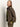 A person with long, straight, light brown hair wears the Sanctuary Clothing barn jacket in burnt olive over a green shirt and green pants, standing against a plain light background and looking slightly past the camera.