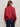 A person with long brown hair and sunglasses faces away from the camera in a Sanctuary Clothing satin track jacket in crimson and dark blue jeans, set against a plain light background.