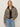 A woman with straight blonde hair and a relaxed expression models the Sanctuary Clothing cropped barn jacket french kitty—a leopard print jacket with a black collar—over a black top and light blue jeans against a plain background.