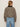 A person with light brown hair, wearing large hoop earrings and light blue jeans, is seen from behind in the Sanctuary Clothing cropped barn jacket french kitty, featuring a leopard print with black collar, against a plain light background.