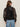 A person with long brown hair wears sunglasses and the Sanctuary Clothing shane organza bomber black jacket with light blue jeans, standing with their back to the camera against a plain light background.
