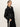 A woman with light hair tied back wears the Sanctuary Clothing coated twill bomber jacket in black and black pants with a white side stripe, standing confidently against a plain white background with one hand in her pocket.