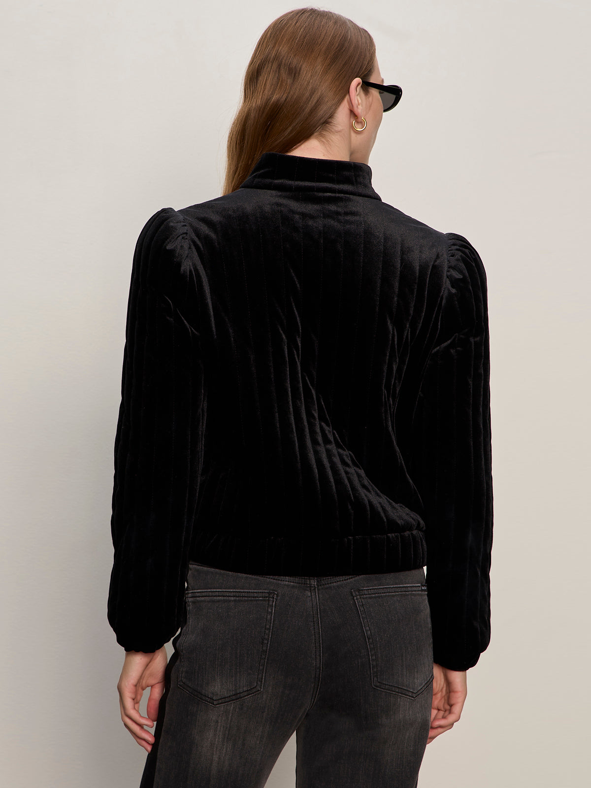 A person with long, light brown hair wears the Sanctuary Clothing quilted velvet jacket in black and dark jeans, standing with their back to the camera against a plain light background.