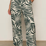 Someone wearing Sanctuary Clothing’s the soft trouser green oasis extended sizing, styled with black sandals and a tucked-in white top, stands against a plain background.
