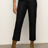 A person in Sanctuary Clothing's the marine jeans after hours—high-waisted black jeans with frayed hems—paired with a white top and tan suede ankle boots, stands against a light-colored wall.
