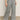 A person stands against a plain background wearing Sanctuary Clothing’s marine full length semi high rise pant in yacht stripe. The gray pinstriped pants are paired with black open-toe sandals; the photo is cropped from the waist down.