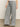 A person wears Sanctuary Clothing's marine full length semi high rise pant yacht stripe with black sandals and a light top, standing on a smooth, light-colored floor against a plain background.