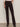 A person stands against a light wall wearing Sanctuary Clothing’s corduroy hayden bootcut pant semi sweet, paired with a light pink top and black boots, with one hand tucked into a front patch pocket.