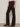 A person wearing Sanctuary Clothing's corduroy hayden bootcut pant in semi sweet stands indoors against a light wall, styled with a light pink top and black heeled ankle boots. Side view from shoulders to feet.