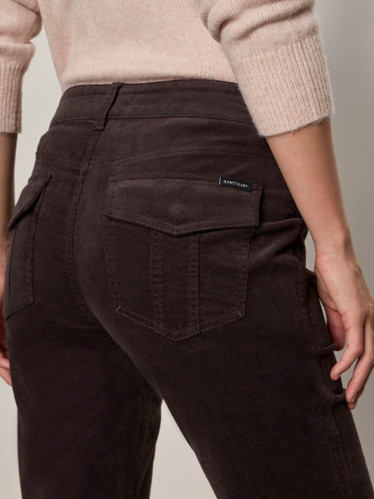 Someone wearing Sanctuary Clothing’s corduroy hayden bootcut pant in semi sweet, featuring back pockets, paired with a light beige sweater; shown from the waist down and viewed from behind.