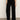 A person wears the Sanctuary Clothing runway ponte trouser in black, paired with black heeled ankle boots, standing against a plain light-colored wall and brown floor. The top half of their body is partially visible.