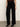 A person wears the Sanctuary Clothing runway ponte trouser in black, paired with black heeled ankle boots, standing against a plain light-colored wall and brown floor. The top half of their body is partially visible.