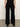 A person is seen from behind, showcasing Sanctuary Clothing's runway ponte trouser in black with heeled shoes against a neutral backdrop—only their lower back, legs, and part of the arms are visible.