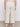 A person stands facing away, wearing high-waisted, wide-leg, off-white pants with two back pockets, a light pink top, and white shoes, against a plain background.