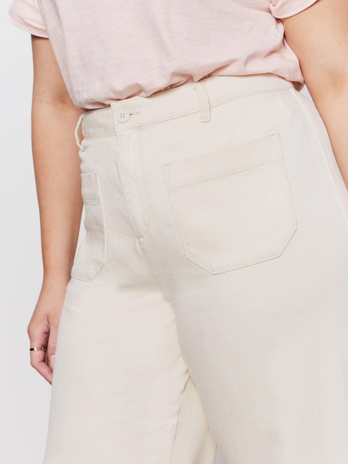 A person wears the Sanctuary Clothing soft marine wide leg crop pant macrame (extended sizing) in cream, featuring visible back pockets, paired with a light pink T-shirt and standing with one arm relaxed by their side.