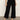 A person models the Sanctuary Clothing soft marine wide leg crop pant in black with black heeled sandals, standing on a concrete floor against a light background. The photo is cropped from the shoulders down.