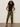 A woman models the Sanctuary Clothing rio pant rambler camo, pairing it with sunglasses, a sleeveless black ribbed top, and black heeled sandals while standing against a plain light-colored background with her hands in her pockets.