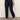 A person wearing Sanctuary Clothing's "cadence 90s straight crop plot twist" jeans in dark blue, paired with a red top and black Mary Jane shoes, stands on a gray floor against a plain light background. Their face is not visible.