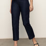 A person wearing Sanctuary Clothing's "cadence 90s straight crop plot twist" jeans in dark blue, paired with a red top and black Mary Jane shoes, stands on a gray floor against a plain light background. Their face is not visible.