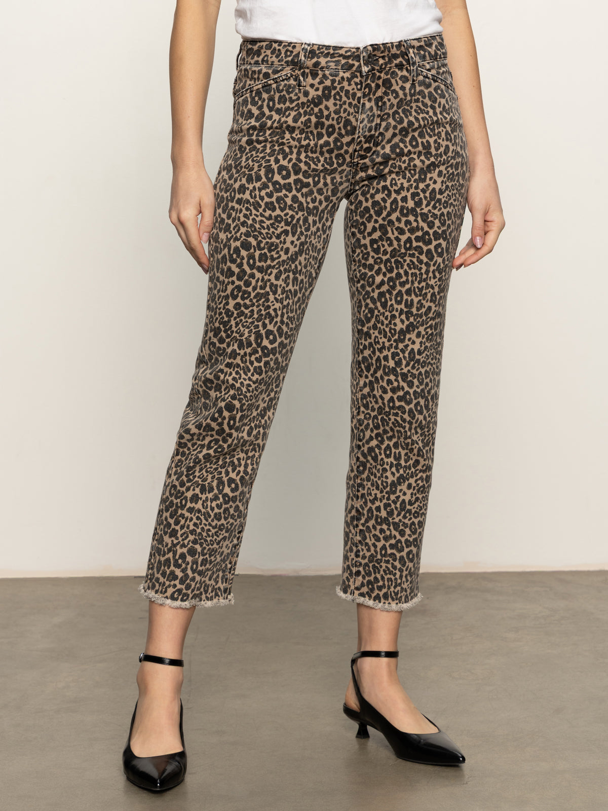 A person wearing Sanctuary Clothing cadence 90 straight crop jeans in french kitty, a white top, and black ankle-strap heels stands on a concrete floor against a plain light background.