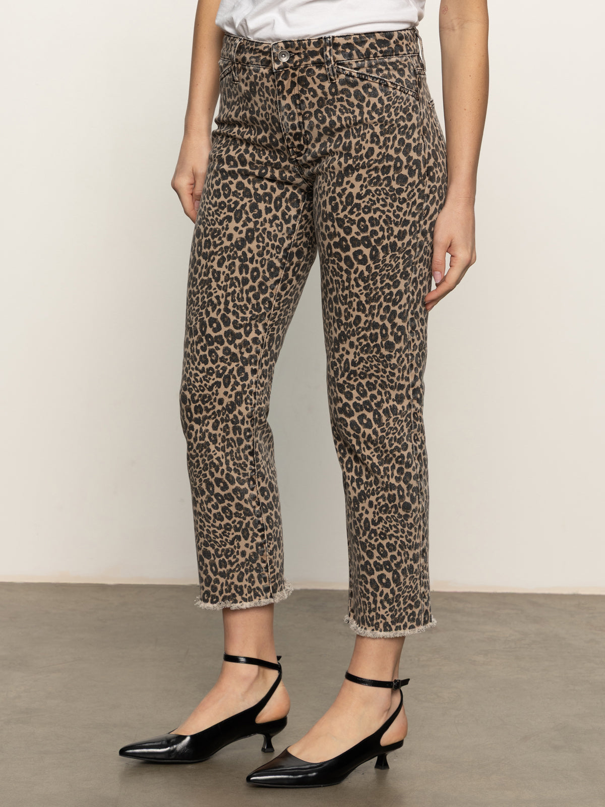 A person wearing Sanctuary Clothing's cadence 90 straight crop jeans in French Kitty, styled with a white top and black low-heeled Mary Jane shoes, stands on a gray concrete floor against a plain background.