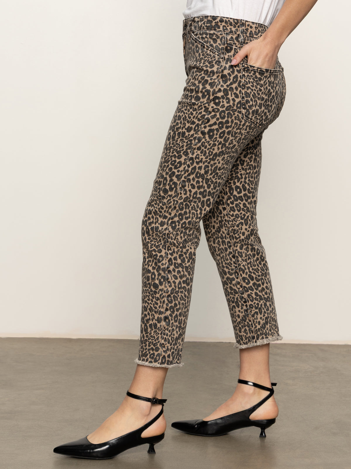 A person stands indoors with a hand in their pocket, wearing Sanctuary Clothing's cadence 90 straight crop jeans in french kitty. Only their body from the shoulders down is visible, paired with a white top and black low-heeled ankle-strap shoes.