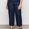 A person stands against a light background wearing Sanctuary Clothing's league crop plot twist extended sizing top, paired with high-waisted dark blue wide-leg jeans with front pockets and black strappy sandals.