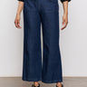 A person wears Sanctuary Clothing's league crop plot twist black textured long-sleeve shirt, paired with dark blue wide-leg jeans with front patch pockets and black strappy sandals, standing against a plain background.